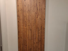 A wooden barn-style sliding door with a dark metal track is mounted on a beige wall. The door features a vertical wood plank design with visible grain and knots, adding a rustic touch to the interior.