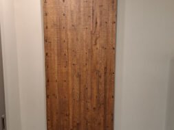 A wooden barn-style sliding door with a dark metal track is mounted on a beige wall. The door features a vertical wood plank design with visible grain and knots, adding a rustic touch to the interior.