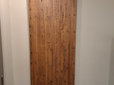 A wooden barn-style sliding door with a dark metal track is mounted on a beige wall. The door features a vertical wood plank design with visible grain and knots, adding a rustic touch to the interior.