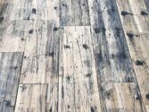 A close-up view of a distressed wooden floor with a pattern of dark stains, scratches, and wear, highlighting the rustic and weathered texture of the planks.