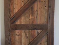 A rustic wooden sliding barn door with a diagonal Z-brace design, made from weathered wood planks, mounted on a metal track against a white wall.