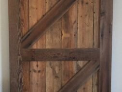 A rustic wooden sliding barn door with a diagonal Z-brace design, made from weathered wood planks, mounted on a metal track against a white wall.