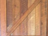 A rustic wooden barn door with vertical planks and a diagonal brace forming a Z pattern. The door displays a natural wood grain and warm brown tones, giving it a vintage, handcrafted appearance.