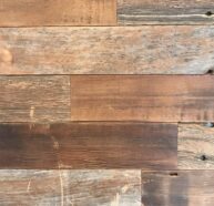 Close-up view of a wooden wall with horizontal planks in various shades of brown, featuring visible grain patterns and small knots. The wood has a rustic, reclaimed look, with some signs of wear and weathering.