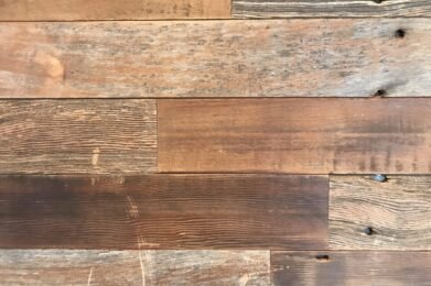 Close-up view of a wooden surface with various shades and textures. The planks are aligned horizontally and show natural grain patterns and knots, creating a rustic appearance.